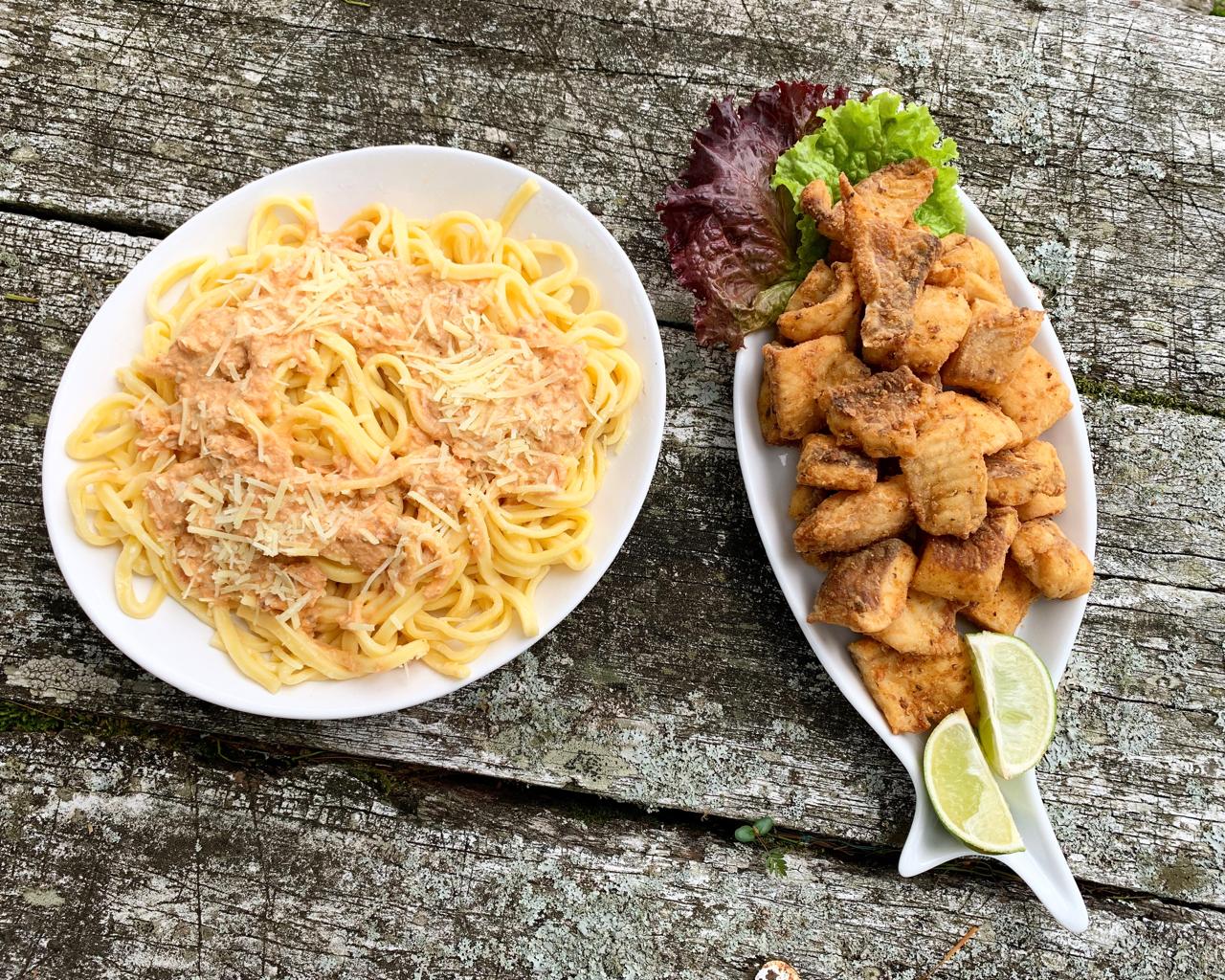 Massa com molho e porção de tilápia frita com limão sobre mesa de madeira