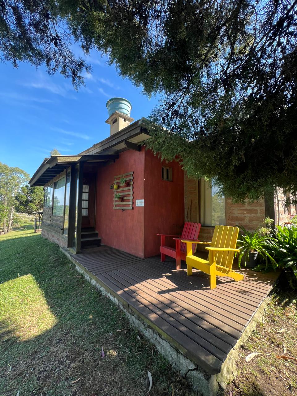 Cabana vermelha com deck de madeira e cadeiras coloridas sob as árvores